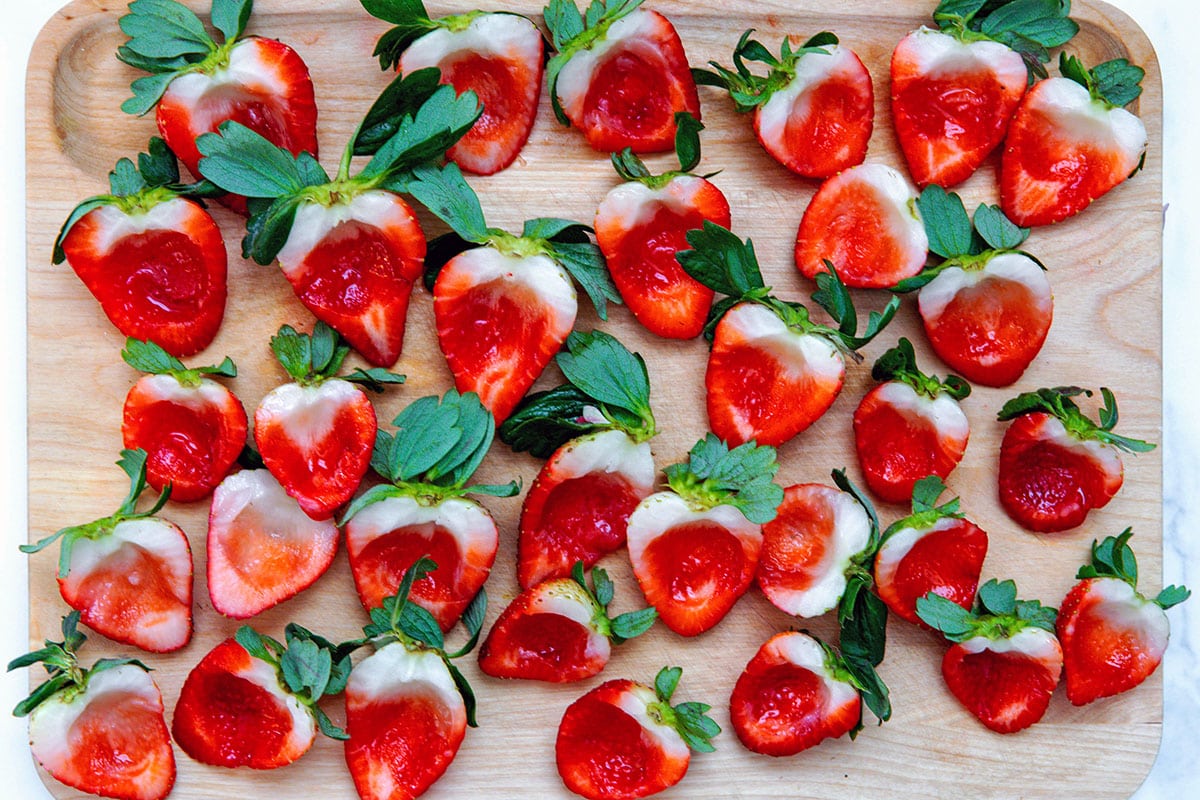 Strawberries cut in half with centers scooped out on a wooden cutting board.