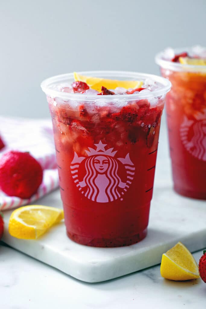 Head-on view of a Starbucks cup of Strawberry Acai Lemonade with strawberries and lemons all around and recipe title at top.