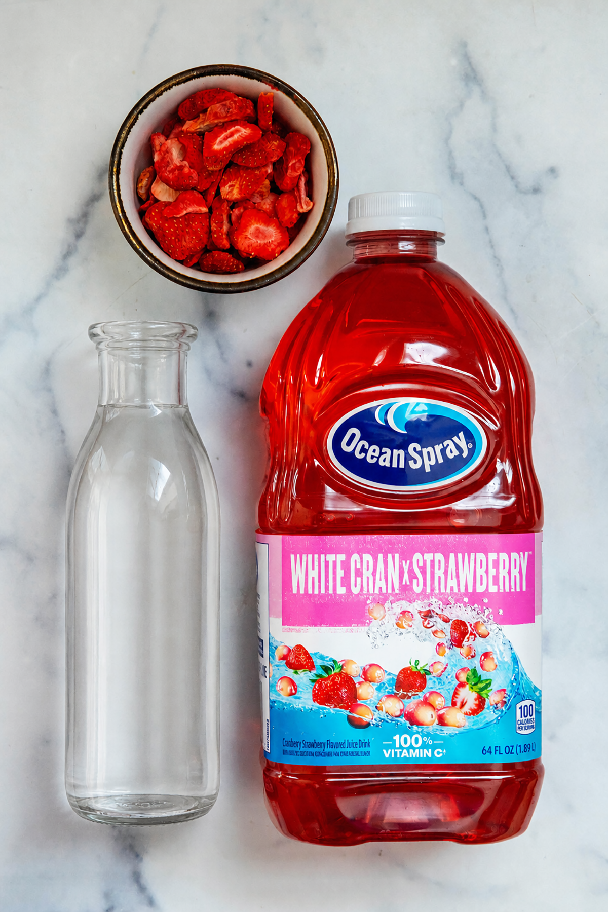 Overhead view of a bottle of White Cran-Strawberry juice, carafe of water, and bowl of freeze-dried strawberries.