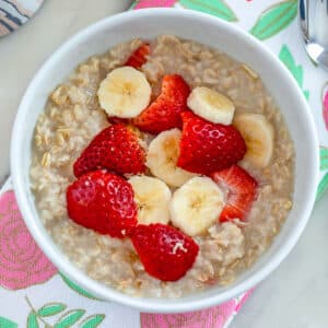 Closeup overhead view of a bowl of strawberry banana oatmeal with fresh berries and slice bananas on top.