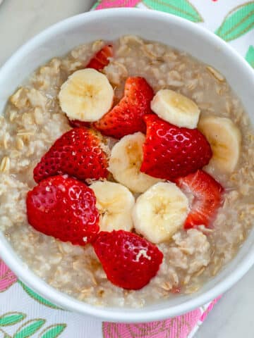 Closeup overhead view of a bowl of strawberry banana oatmeal with fresh berries and slice bananas on top.