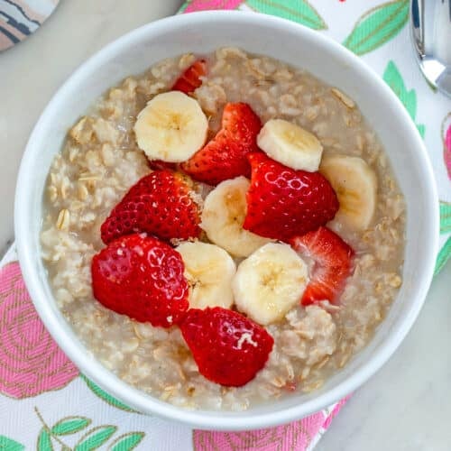 Closeup overhead view of a bowl of strawberry banana oatmeal with fresh berries and slice bananas on top.
