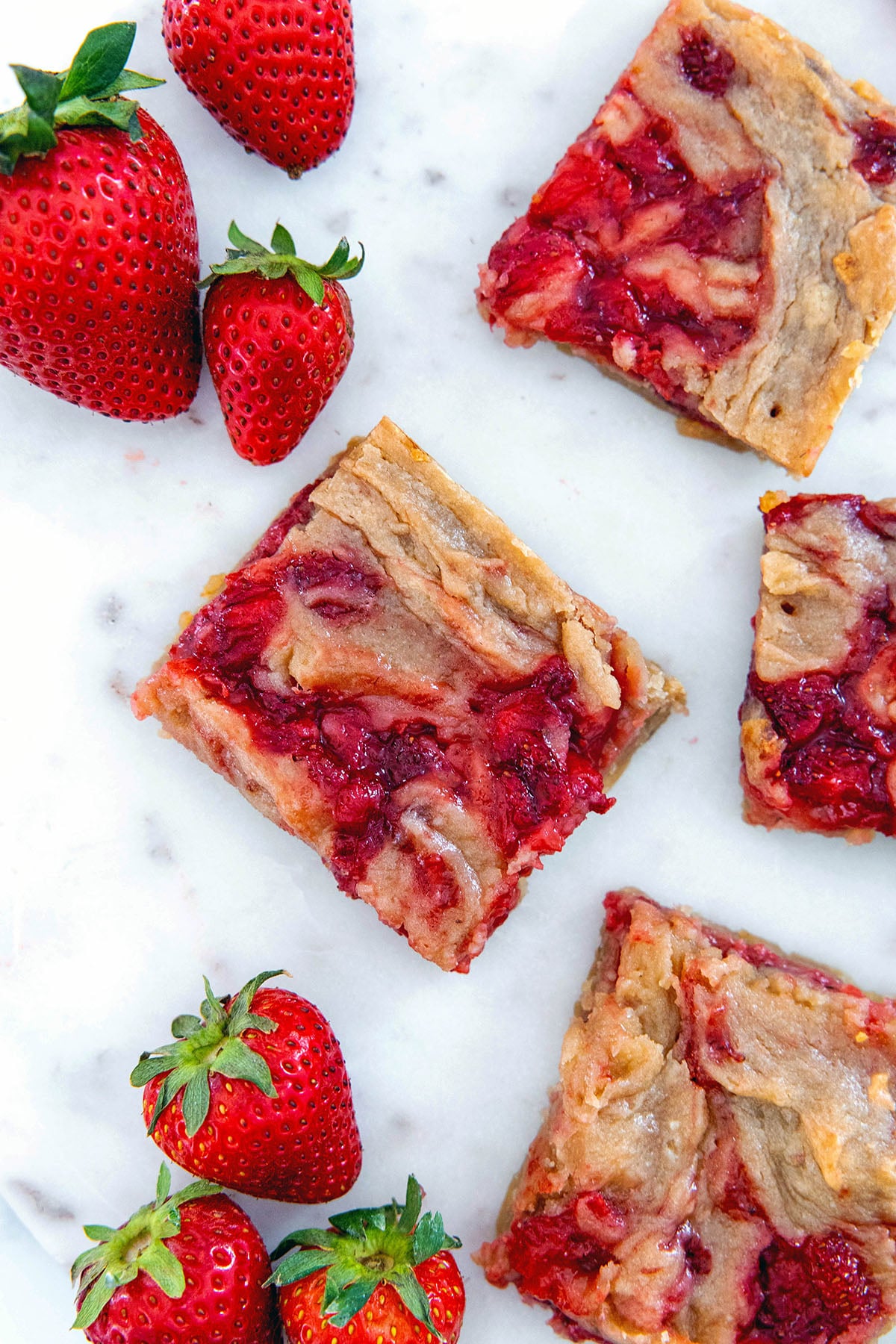 Overhead view of a strawberry brownie on a marble platter with more brownies all around along with fresh strawberries.