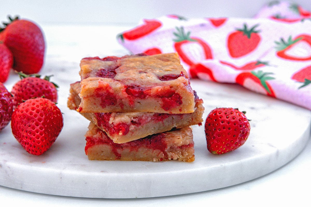 Head-on view of three strawberry brownies stacked on top of each other with whole strawberries all around.