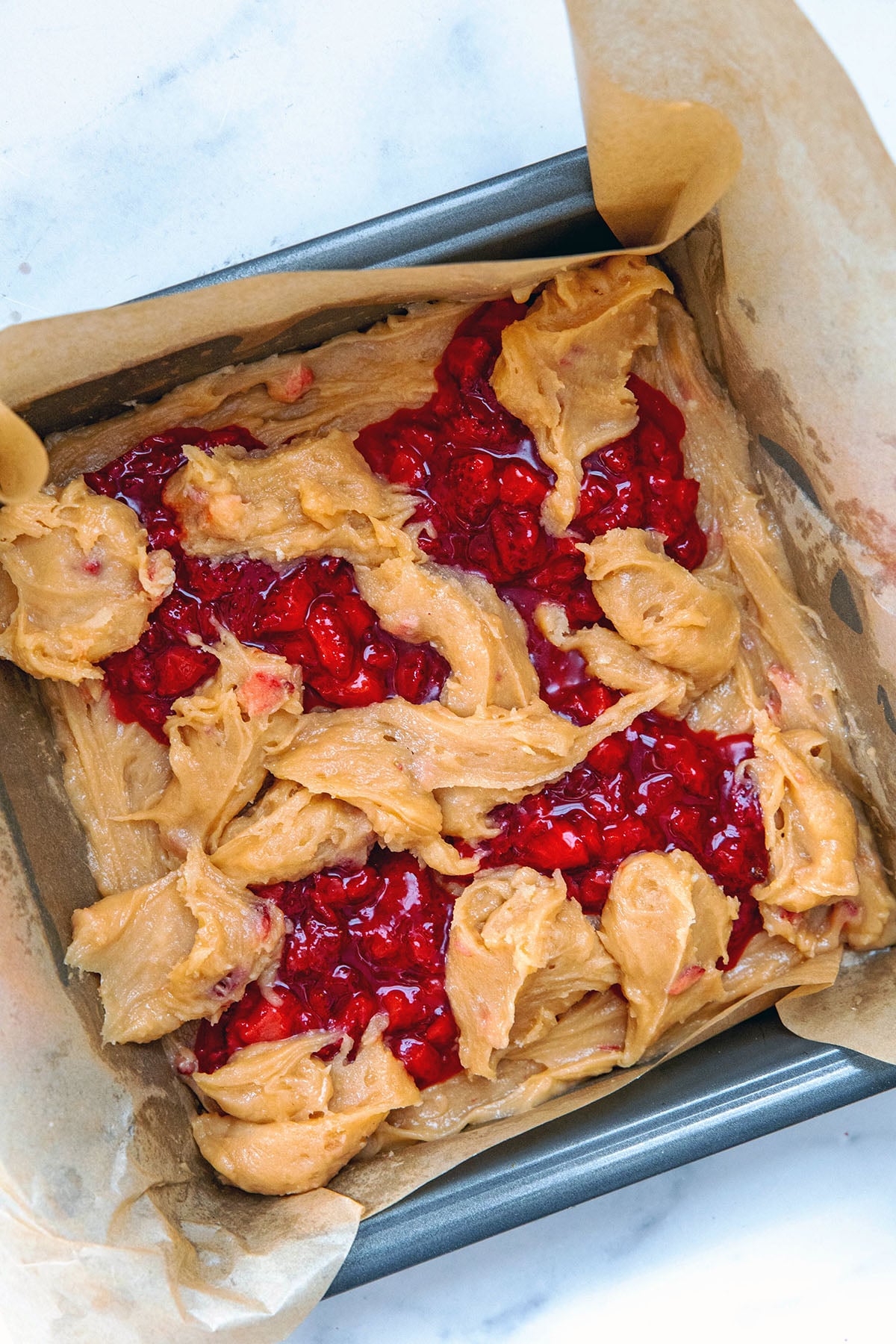 Strawberry brownie batter and strawberry jam in baking pan.