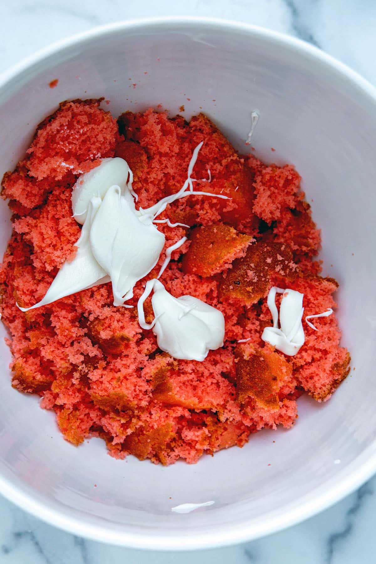 Crumbled up strawberry cake and vanilla icing in a mixing bowl.