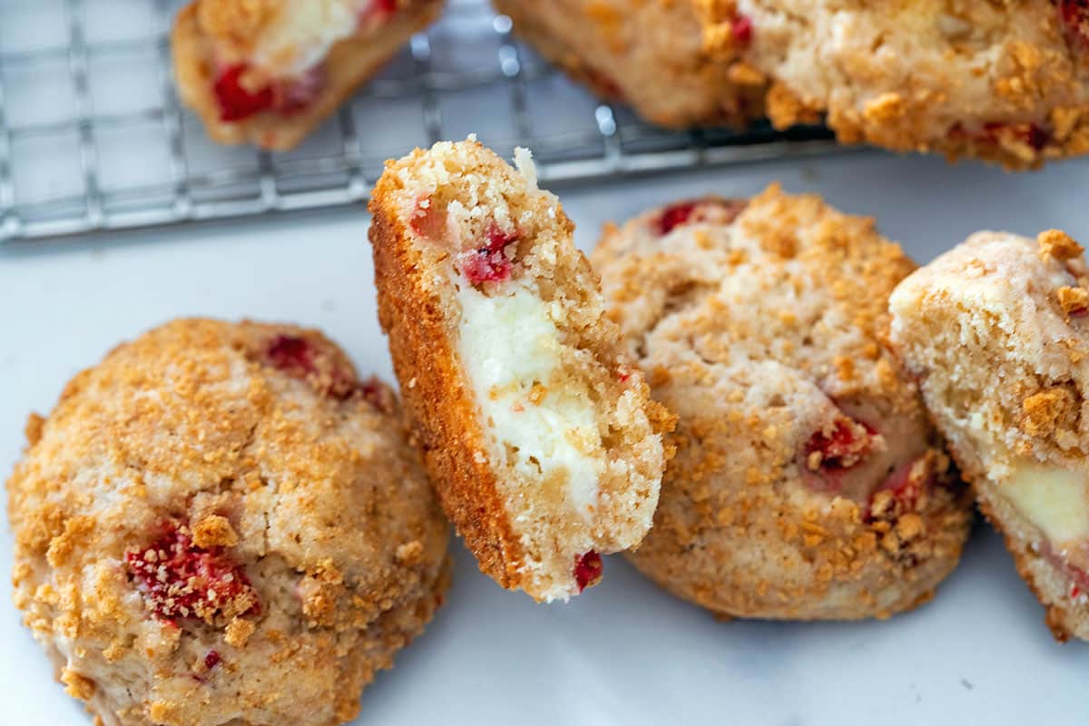Landscape view of strawberry cheesecake cookies with one cut open to show cream cheese middle.