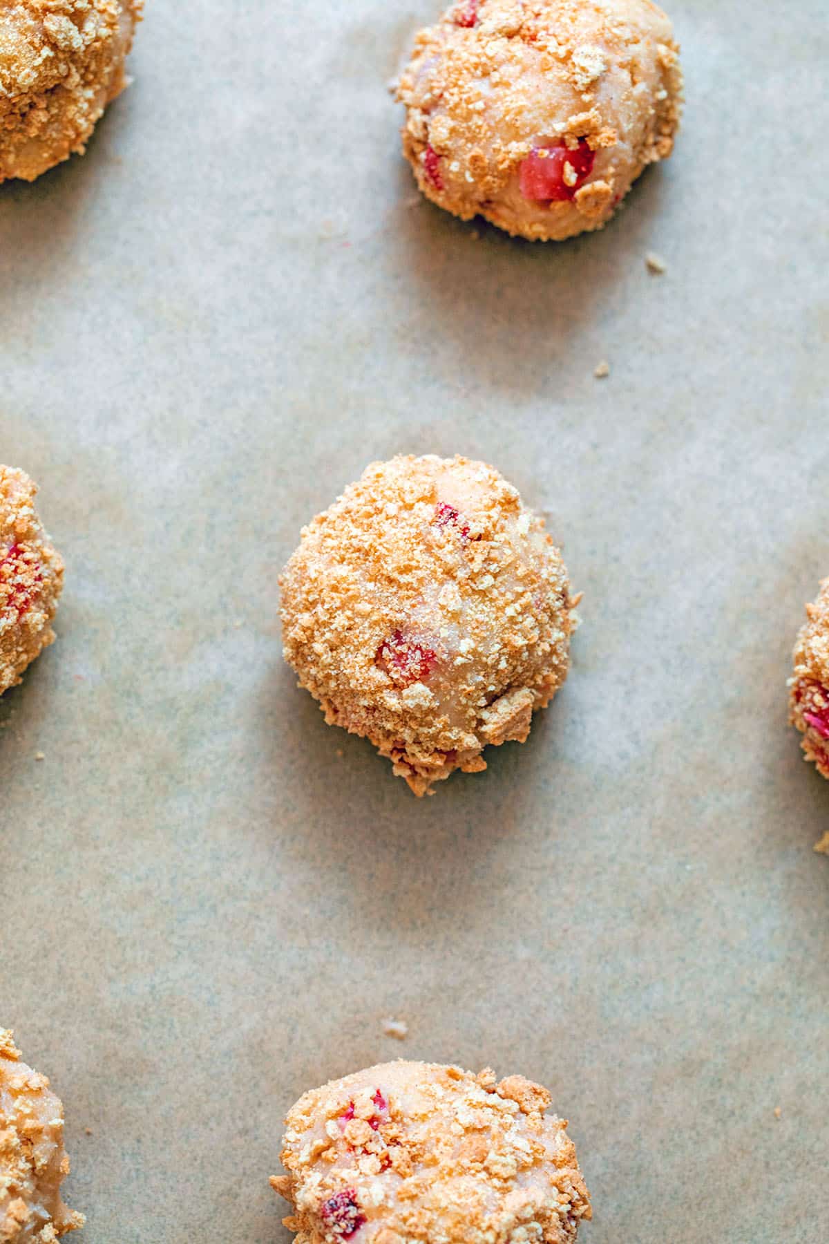 Strawberry cheesecake cookie balls rolled in graham cracker crumbs on baking sheet.