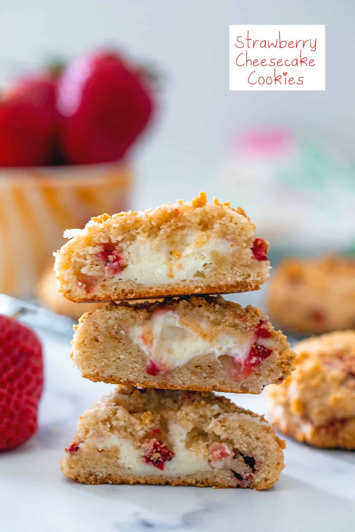 Head-on view of a stack of strawberry cheesecake cookies with cream cheese in the middle with fresh strawberries in the background and recipe title at top.