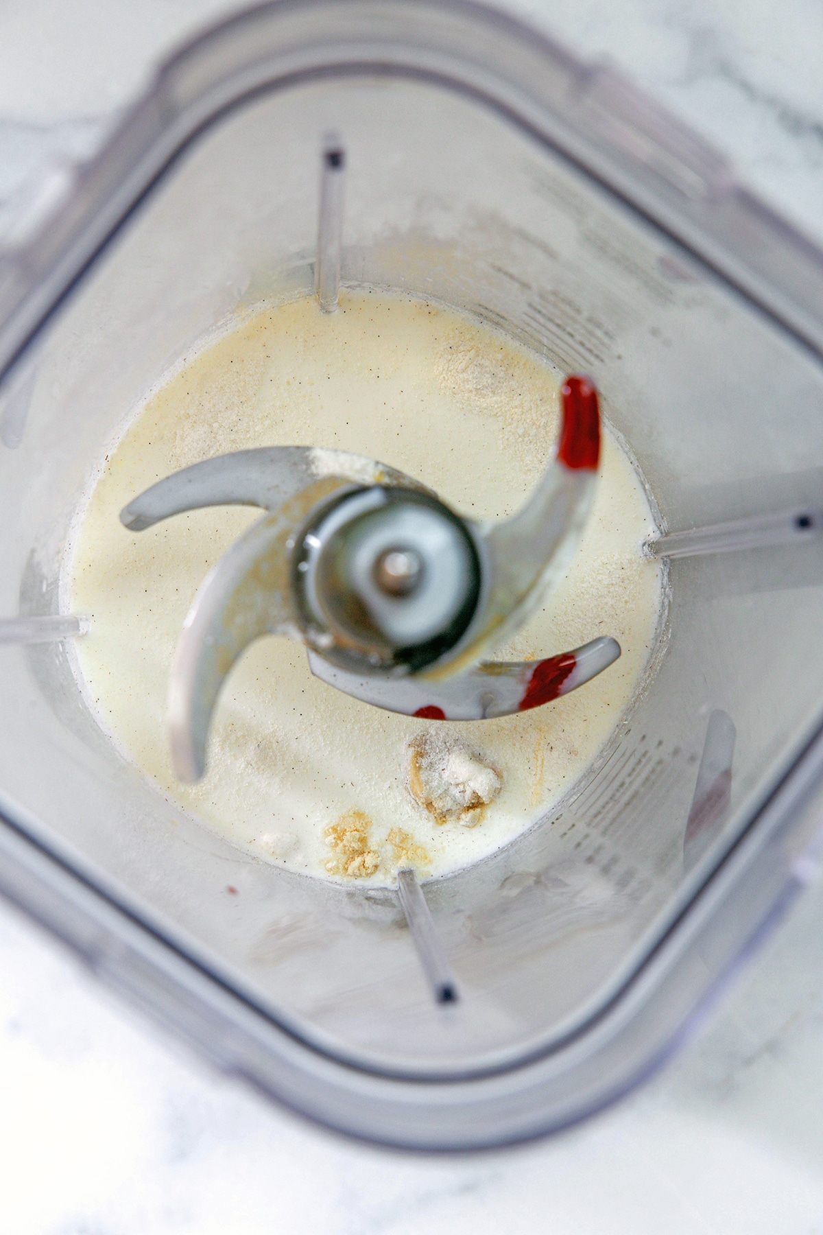 Overhead view of the ingredients for a strawberry cheesecake frappuccino in a blender, including milk, strawberry puree, and xanthan powder.