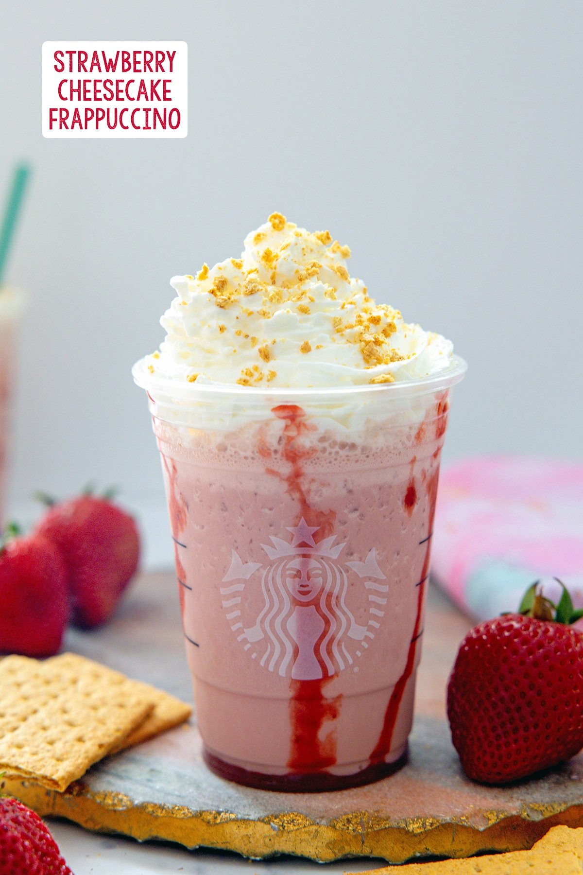 Strawberry cheesecake Frappuccino with whipped cream with strawberries and graham crackers all around and recipe title at top.