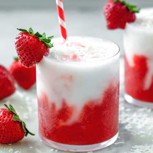 Closeup view of a layered strawberry coconut daiquiri with fresh strawberry garnish and straw.