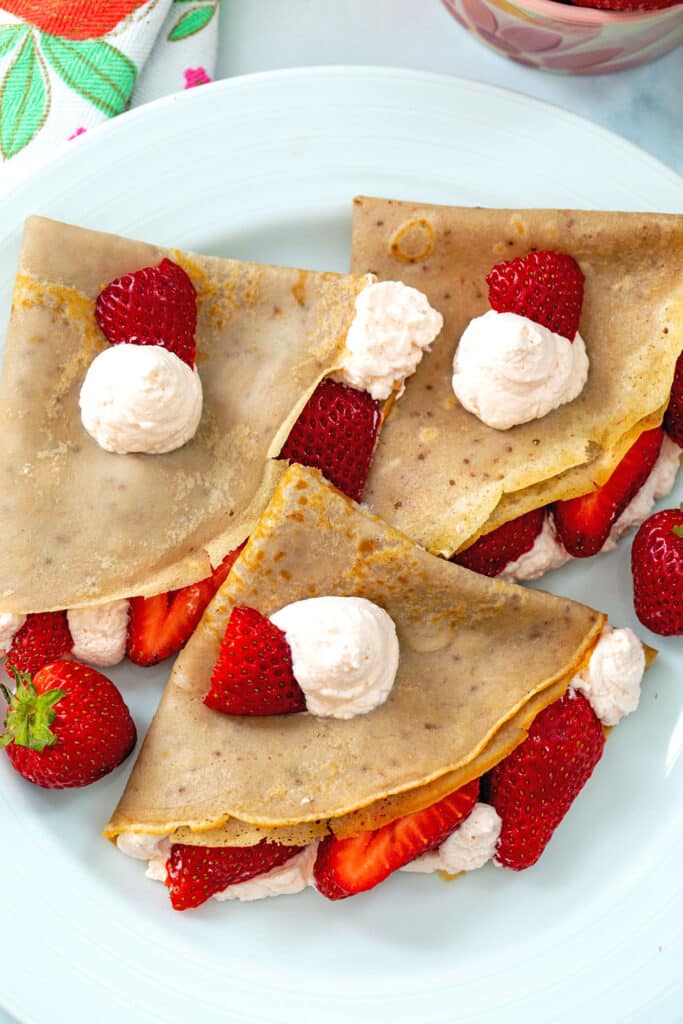 Closeup view of crepes folded over with strawberry whipped cream and sliced strawberries.