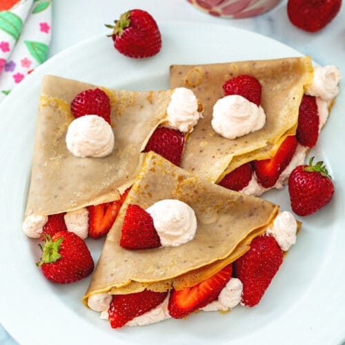 Three strawberry crepes with whipped cream and sliced berries.