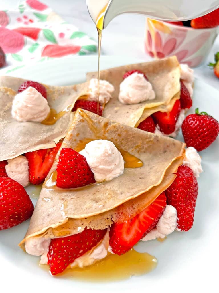 Strawberry crepes with maple syrup being drizzled over the top.