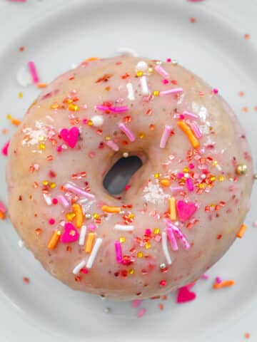 Overhead closeup view of a strawberry frosted donut with sprinkles.