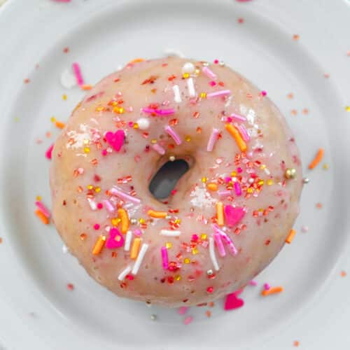 Overhead closeup view of a strawberry frosted donut with sprinkles.