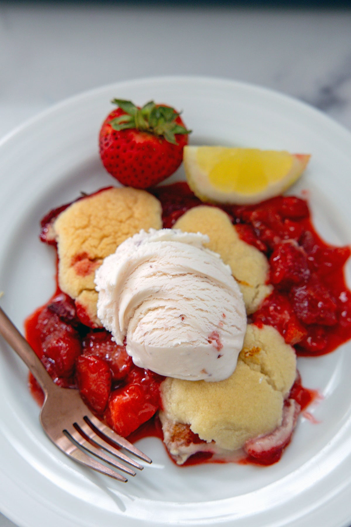 Closeup view of a strawberry cookie cobbler with scoop of strawberry ice cream and a fork.