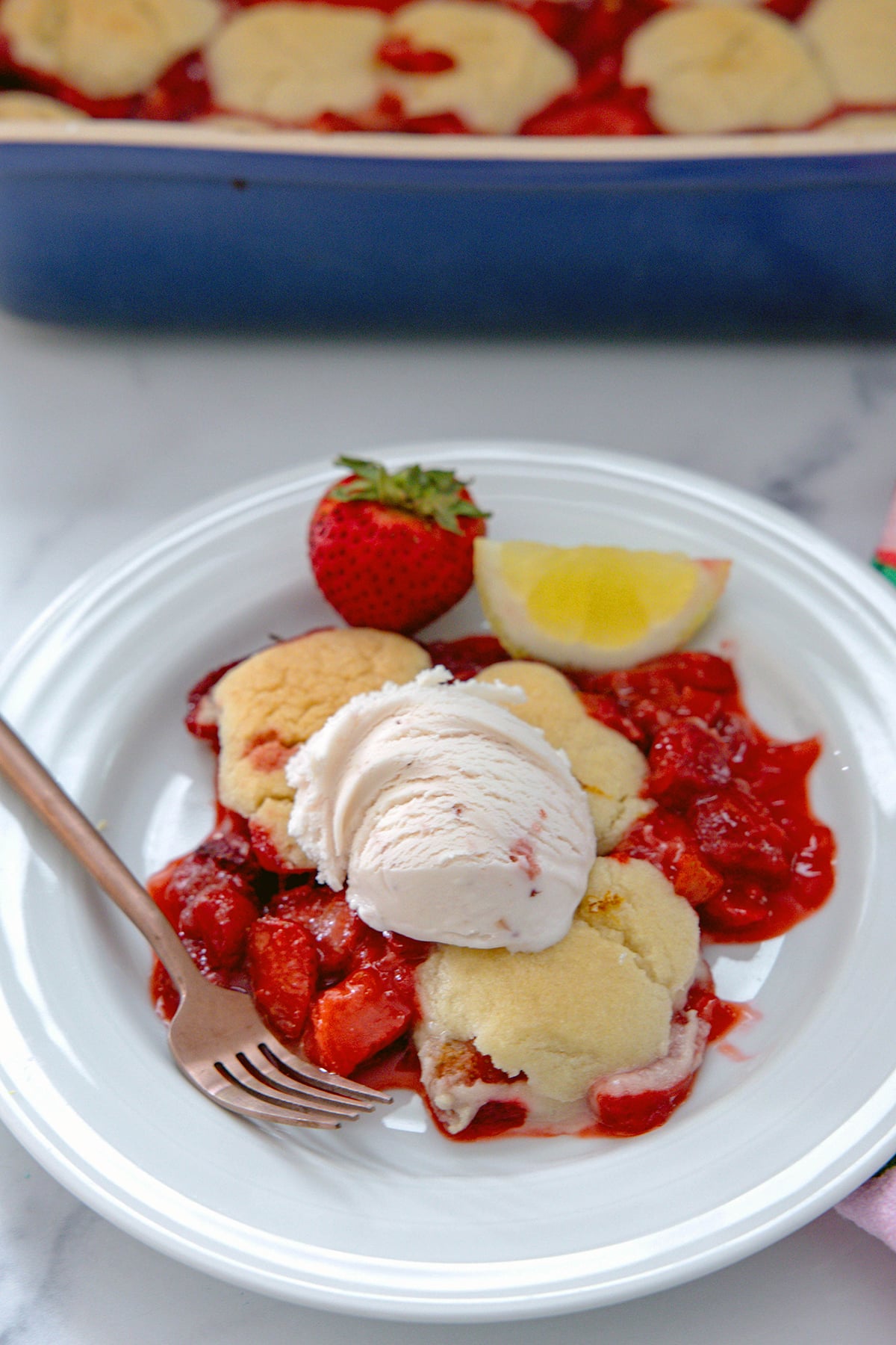 Strawberry lemonade cobbler on a plate topped with strawberry ice cream with recipe title at top of photo.