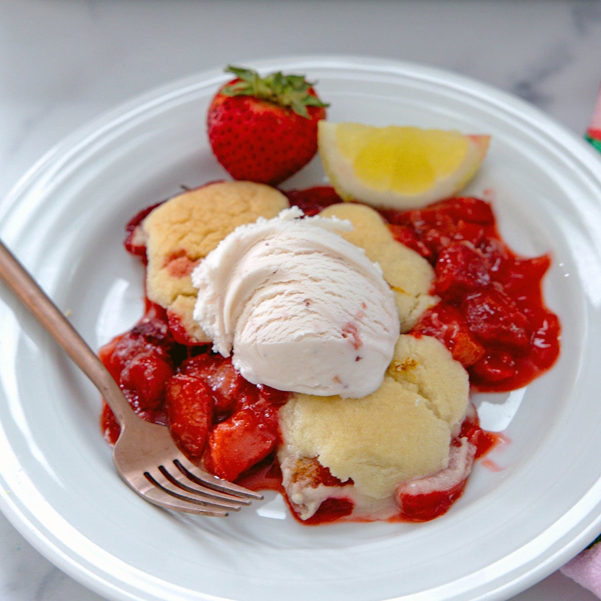 Closeup view of strawberry lemonade cookie cobbler on a white plate with scoop of strawberry ice cream.