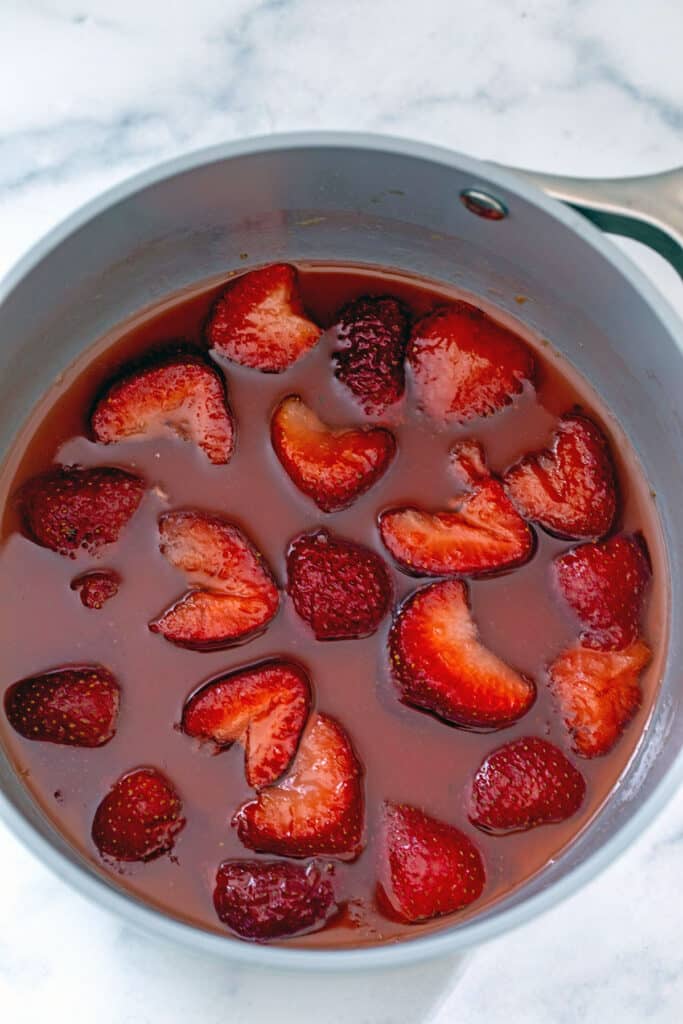 Overhead view of sliced strawberries in syrup in saucepan.