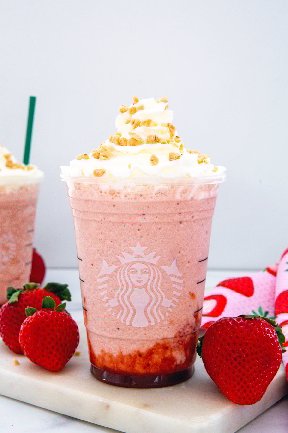 Head-on view of a Strawberry Shortcake Frappuccino in a Starbucks cup with whipped cream and with strawberries all around.