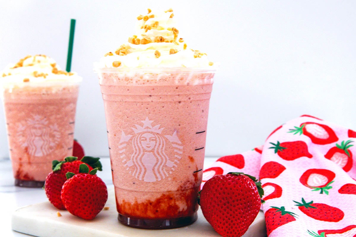 Landscape head-on view of two Strawberry Shortcake Frappuccinos with fresh whole strawberries around.
