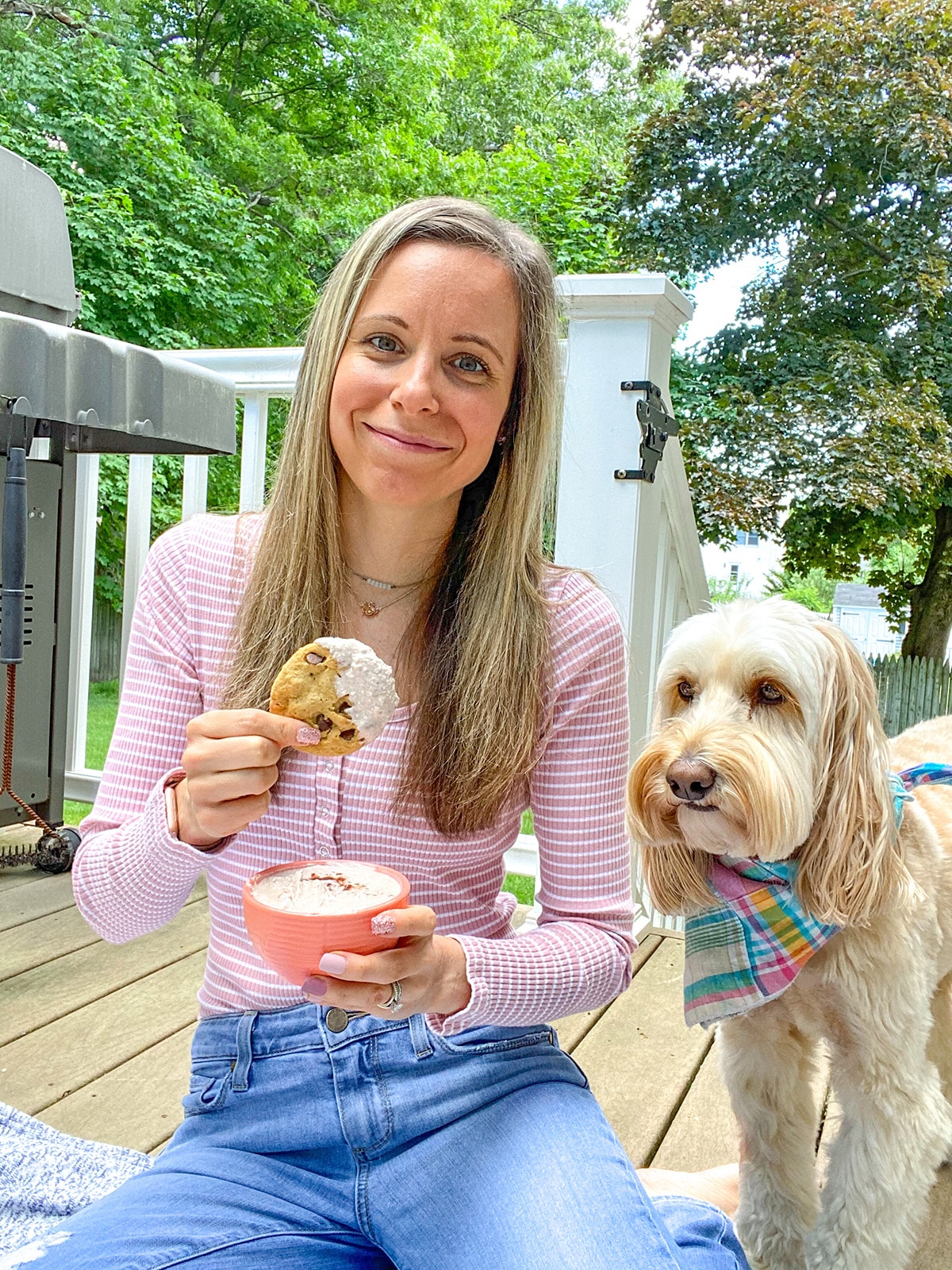 Sues dipping a cookie into cinnamon dip with Winnie the labradoodle next to her.