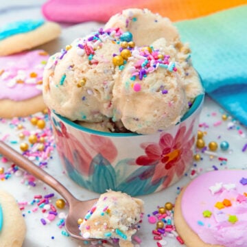 Closeup view of a bowl of sugar cookie dough with sprinkles and a spoonful of cookie dough in front.