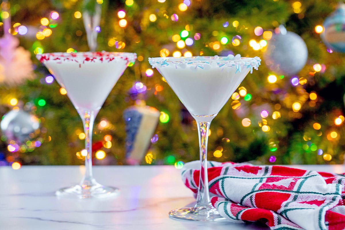 Head-on landscape view of sugar two sugar cookie martinis in front of a lit Christmas tree.