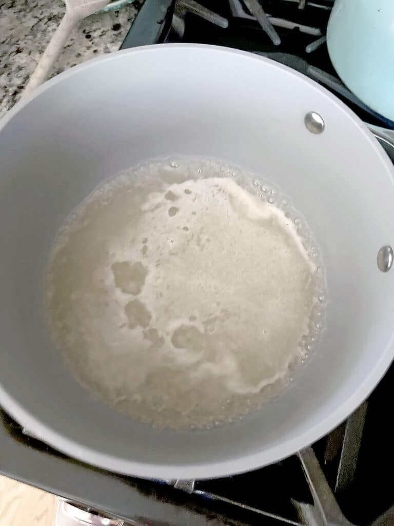 Overhead view of a saucepan with water, lemon juice, and sugar simmering.