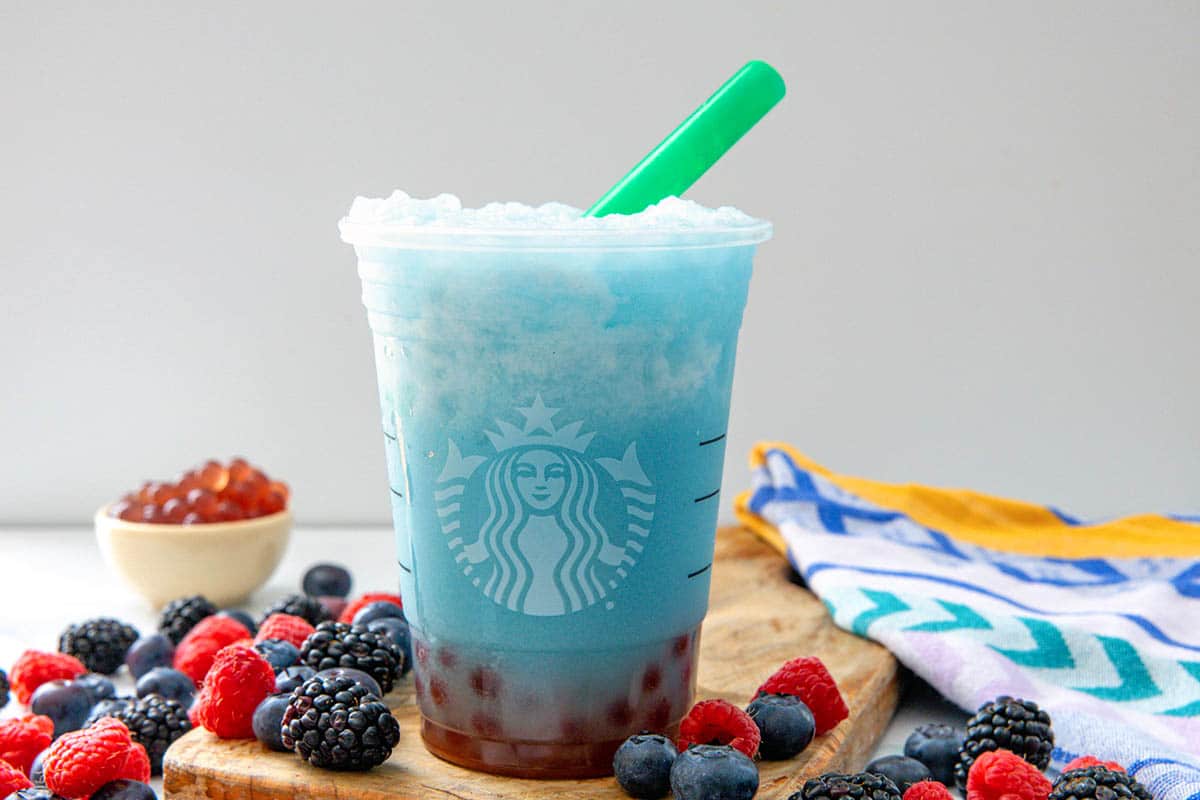 Landscape head-on view of a Summer Skies Drink with fresh berries all around and small bowl of raspberries pearls in background.