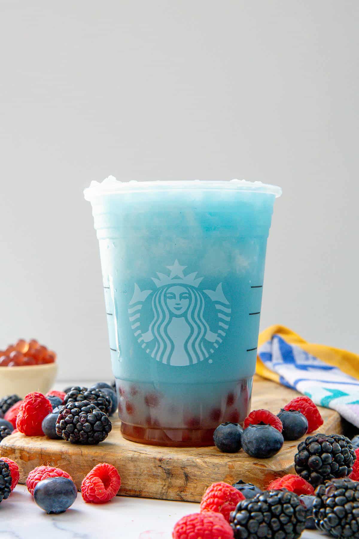 Head-on view of a Summer Skies Drink on a wooden board with raspberries, blackberries, and blueberries all around.