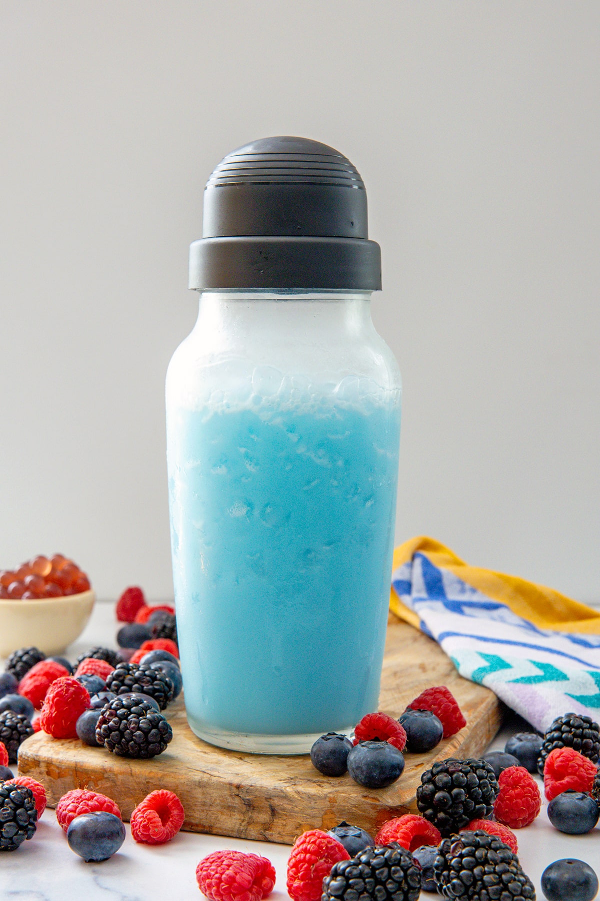 Summer Skies Drink in clear shaker with berries all around.