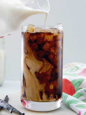 Closeup view of vanilla sweet cream being poured into iced coffee.