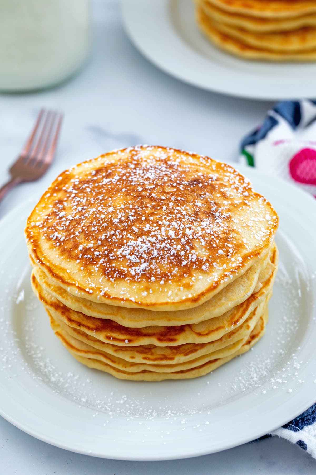 Stack of sweet cream pancakes topped with powdered sugar.