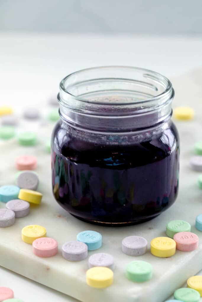 Purple Sweet Tart syrup in a small mason jar with candies all around.