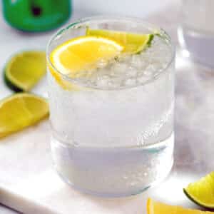 Closeup view of a glass of tequila and Sprite with lemon and lime wedges.
