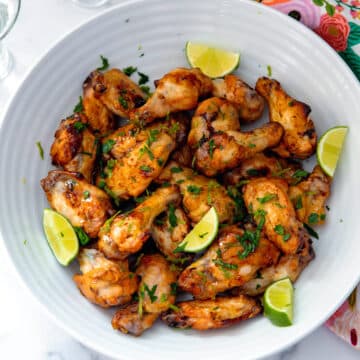 Closeup view of tequila lime chicken wings with lime wedges and chopped cilantro.