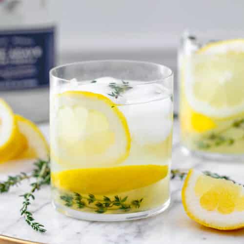 Closeup view of a glass of tequila thyme lemonade with fresh time and lemon slices.