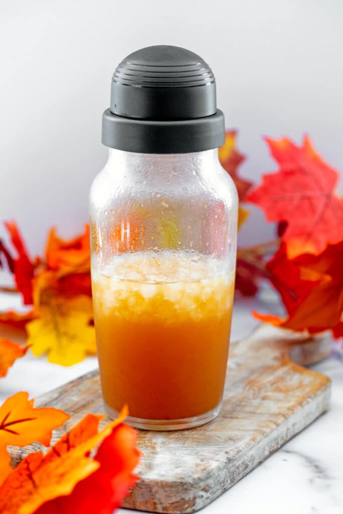 A clear shaker with tequila, apple cider, and pumpkin spice syrup in it with fall leaves all around.
