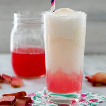 Closeup view of a pink and white rhubarb ice cream soda with a jar of rhubarb syrup in background.