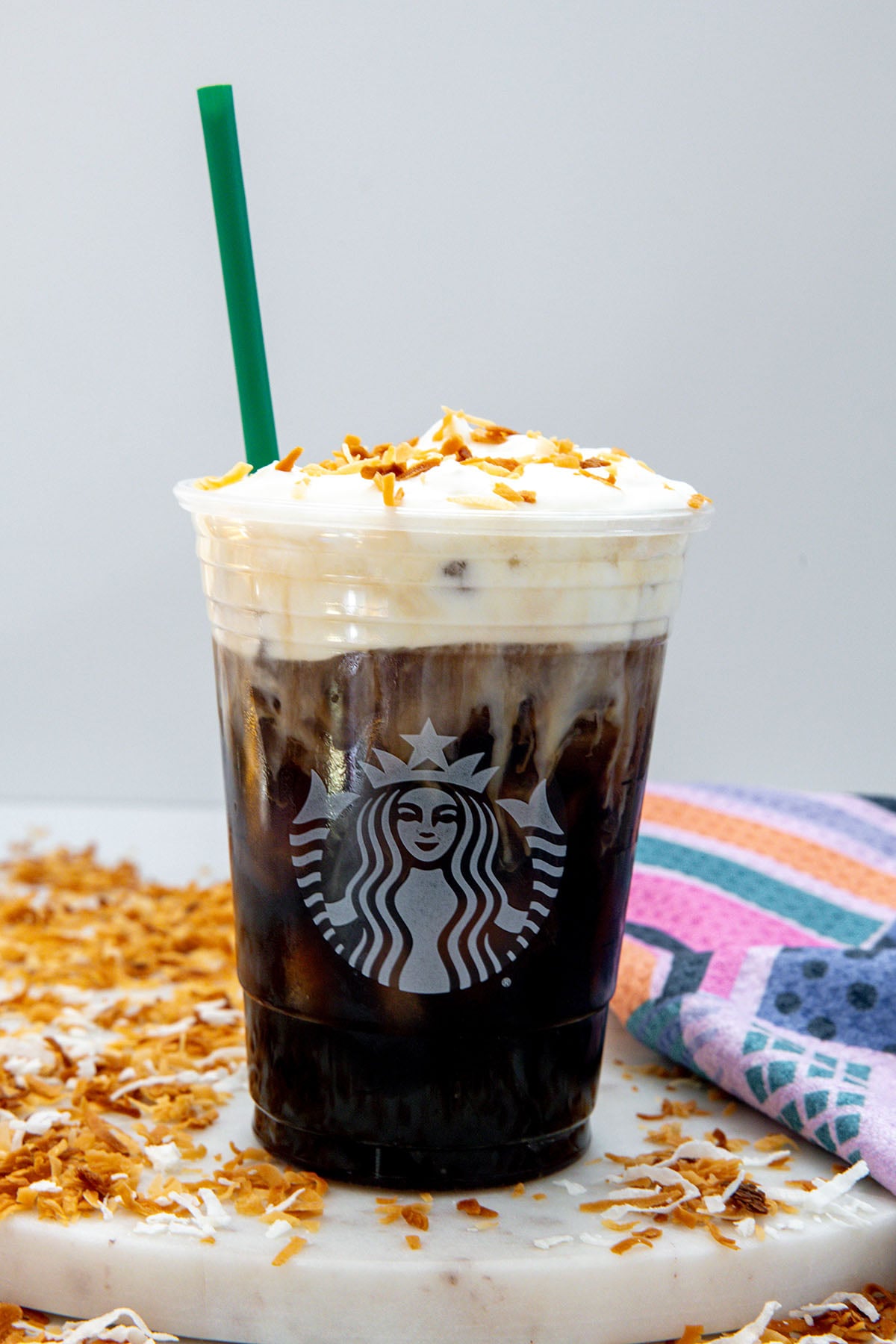 Head-on view of a Starbucks cup of cold brew topped with cold foam and toasted shredded coconut with coconut flakes all around.