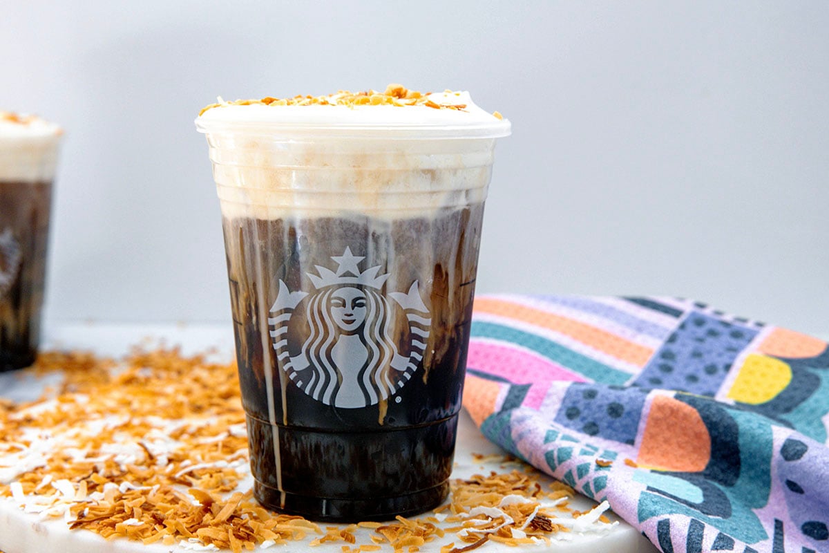 Landscape head-on view of a Starbucks cup of toasted coconut cream cold brew with toasted coconut all around.