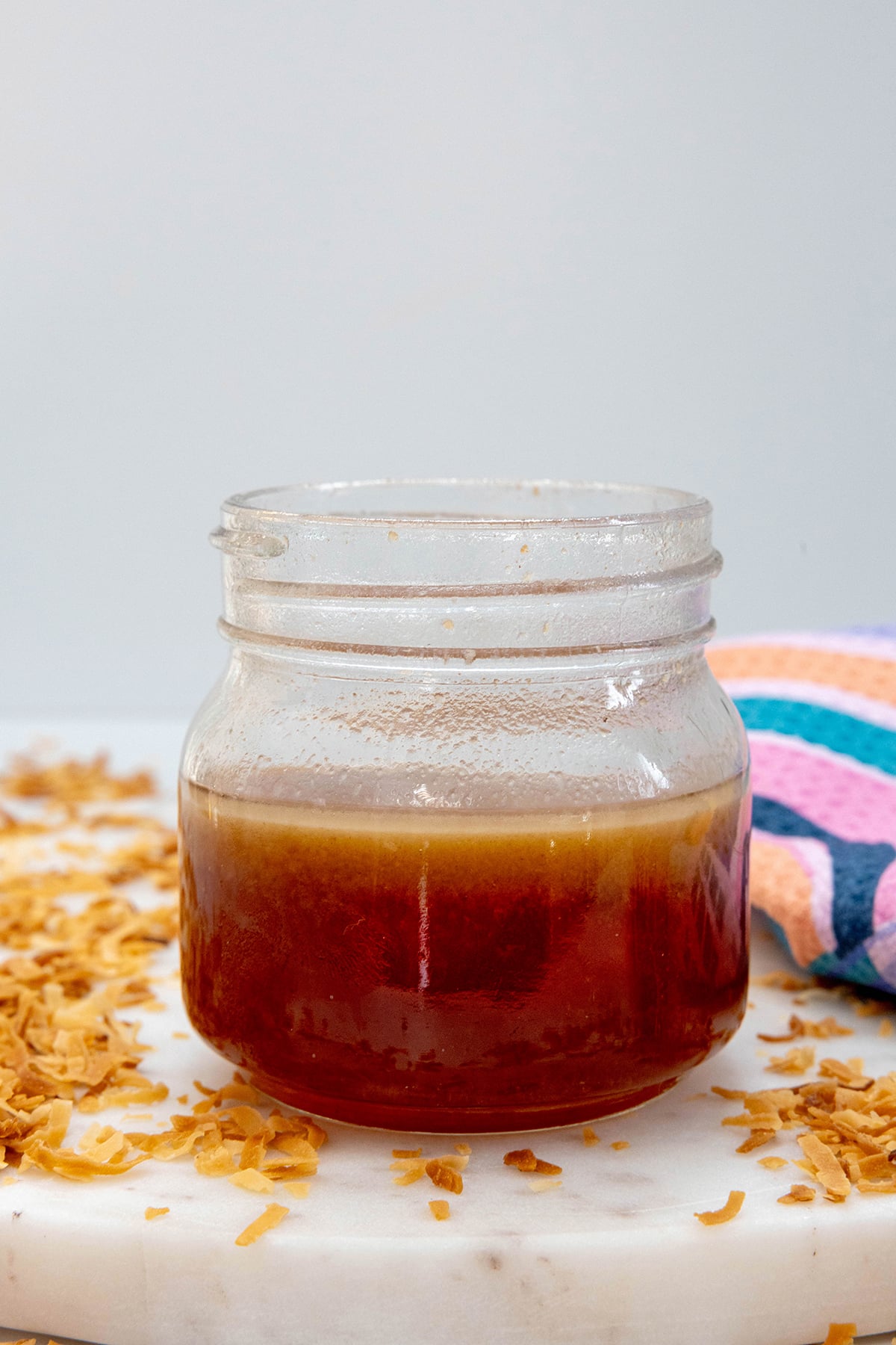 Head-on view of a small jar of toasted coconut syrup with toasted coconut all around.