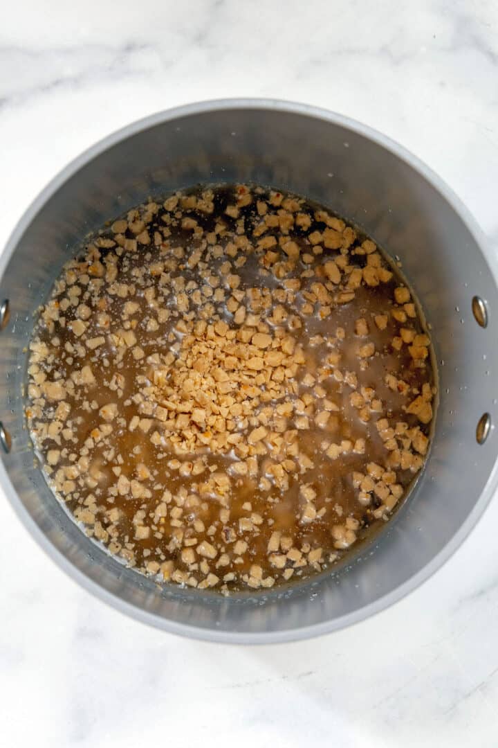 Overhead view of toffee pieces in saucepan with brown sugar and water.