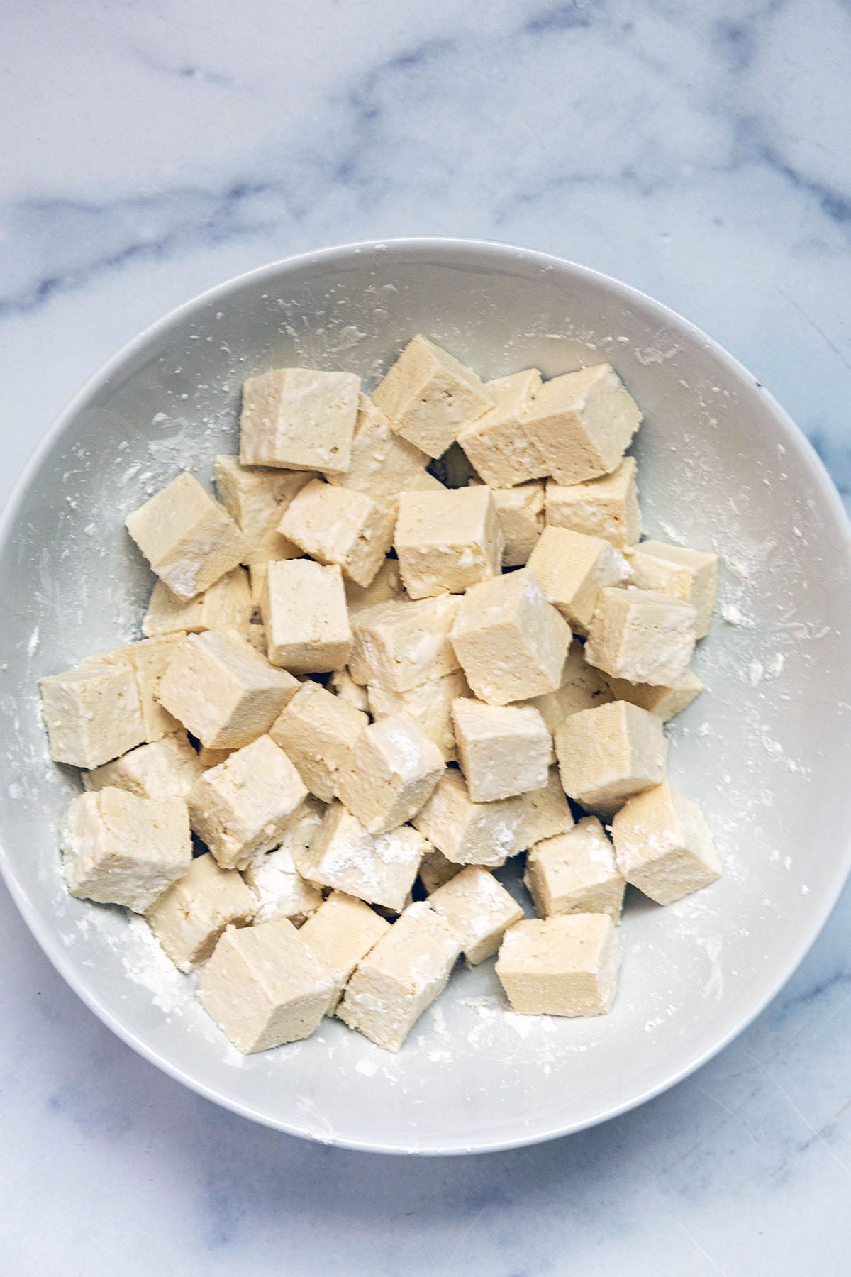 Tofu mixed with cornstarch in bowl.