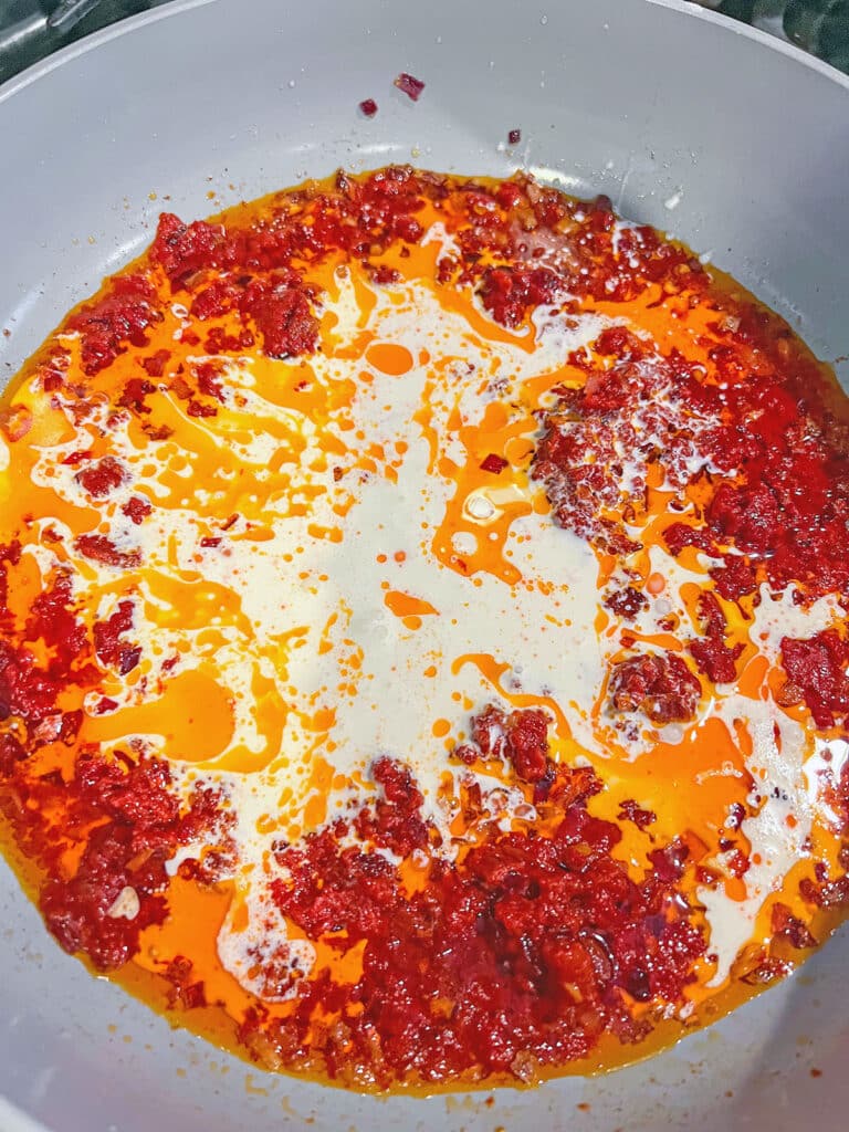 Cream added to tomato vodka pasta sauce in skillet.