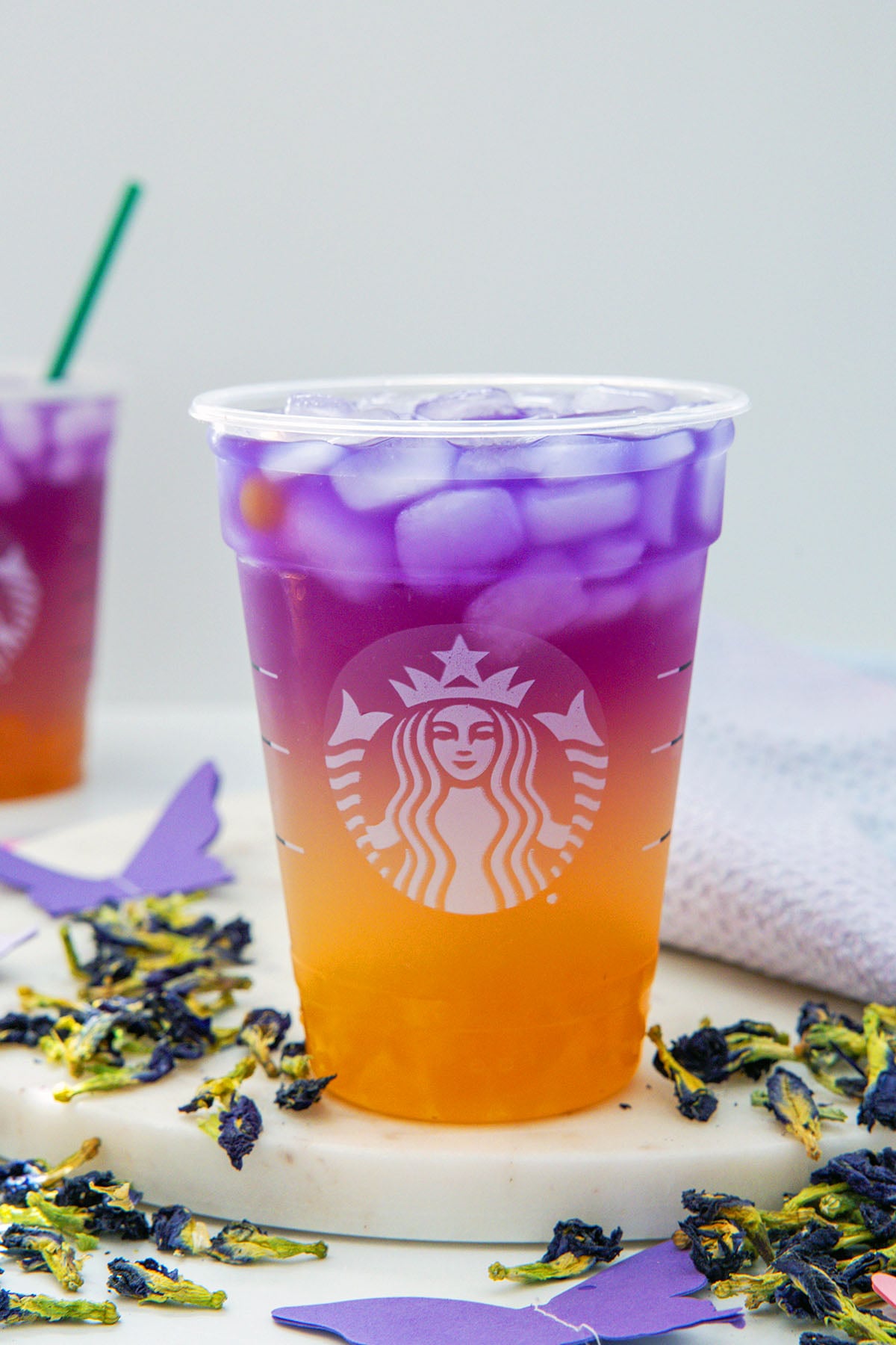 Head-on view of a Tropical Butterfly Refresher in a Starbucks cup with butterfly pea flowers all around.