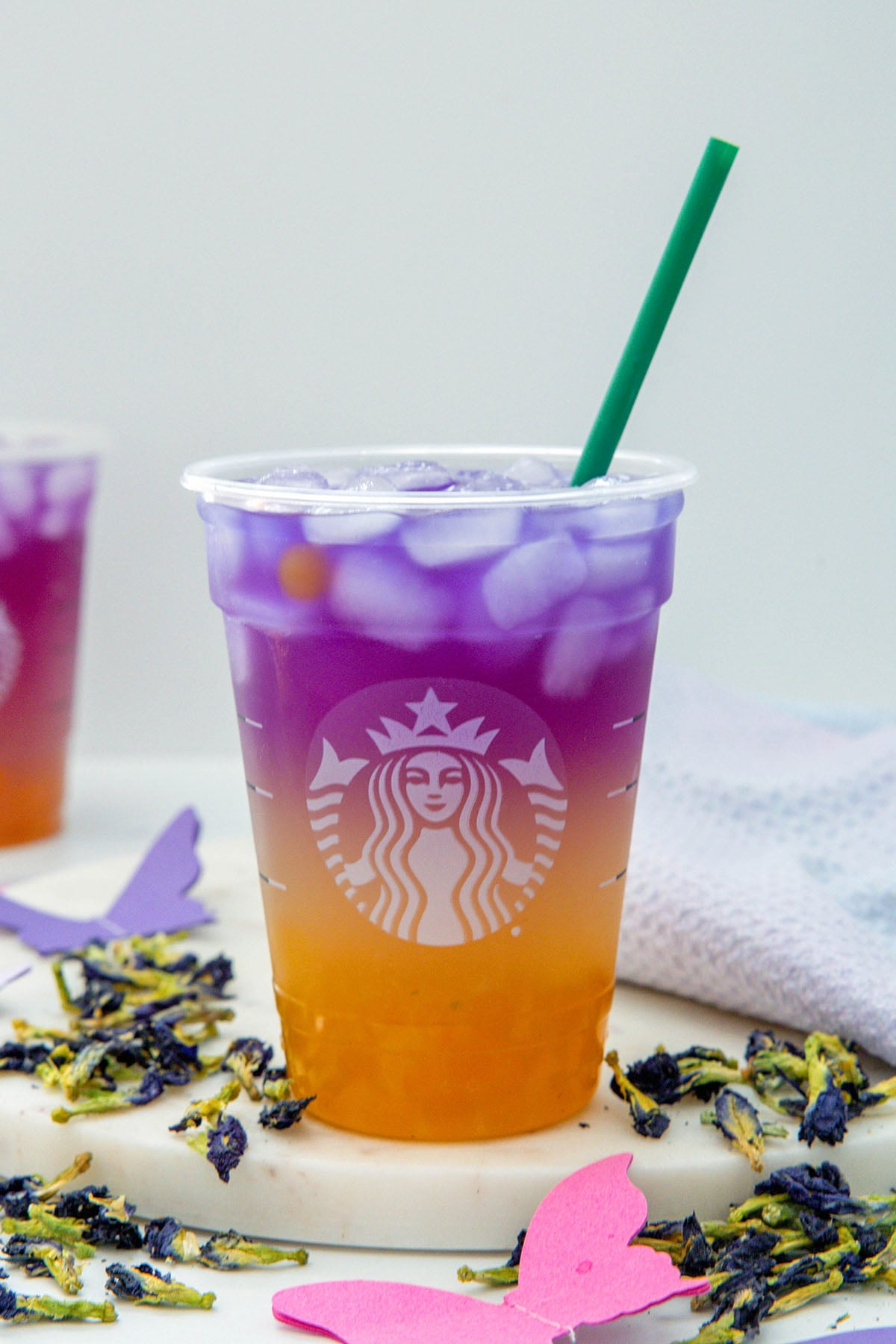 Head-on view of an orange and purple Tropical Butterfly Refresher with green straw and butterfly pea flowers all around.